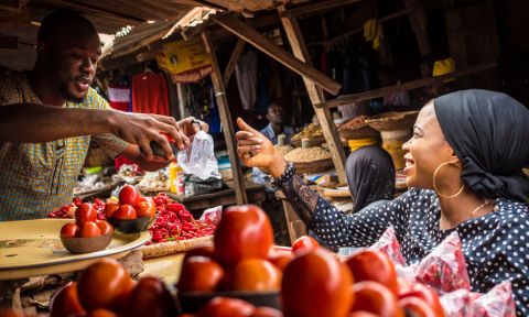 A woman speaks with a vegetable seller in a market.