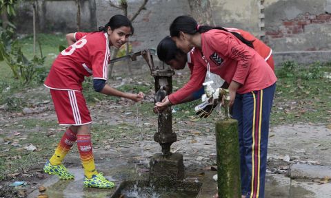 Three teen girls in athletic clothes wash hands at an outdoor pump