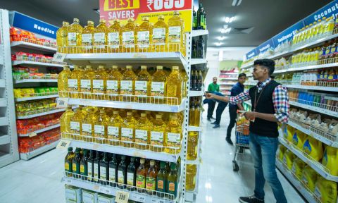 Bottles of vegetable oil on supermarket shelves; shopper standing to right
