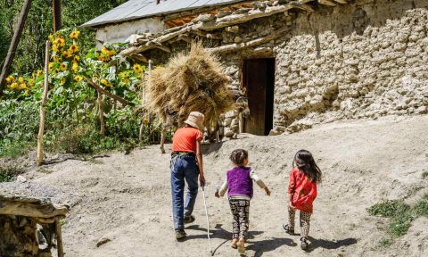 Three children walking uphill toward house with thatched roof