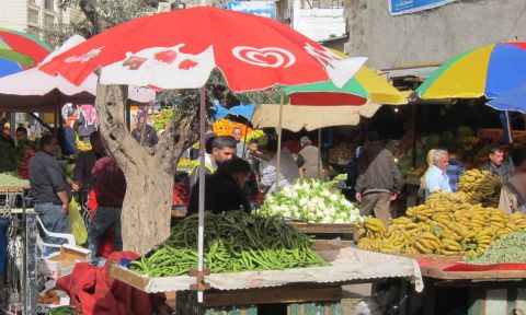Fruits and vegetables on carts, one with a red umbrella, with people