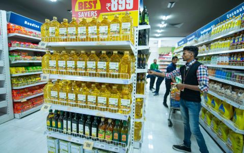Bottles of vegetable oil on supermarket shelves; shopper standing to right