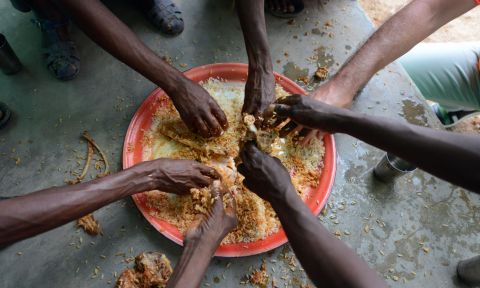 Several hands reach for a bowl of food.