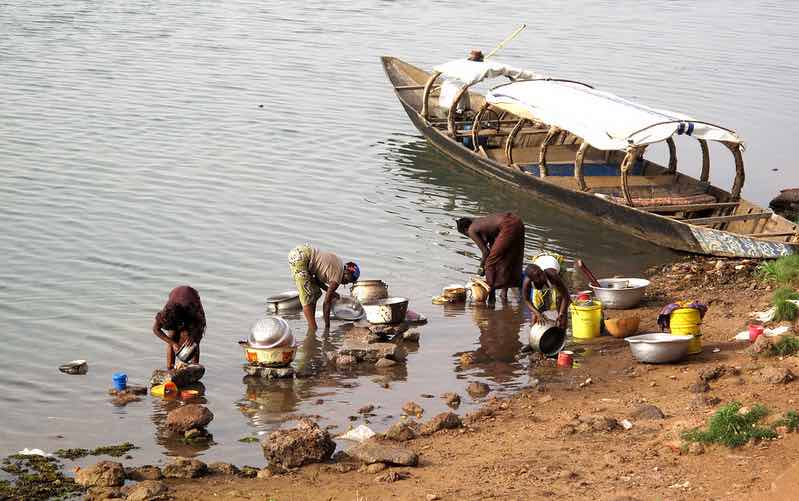 Women washing pans in the river next to a boat with canopy