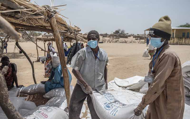 Two men in face masks carry food aid bags