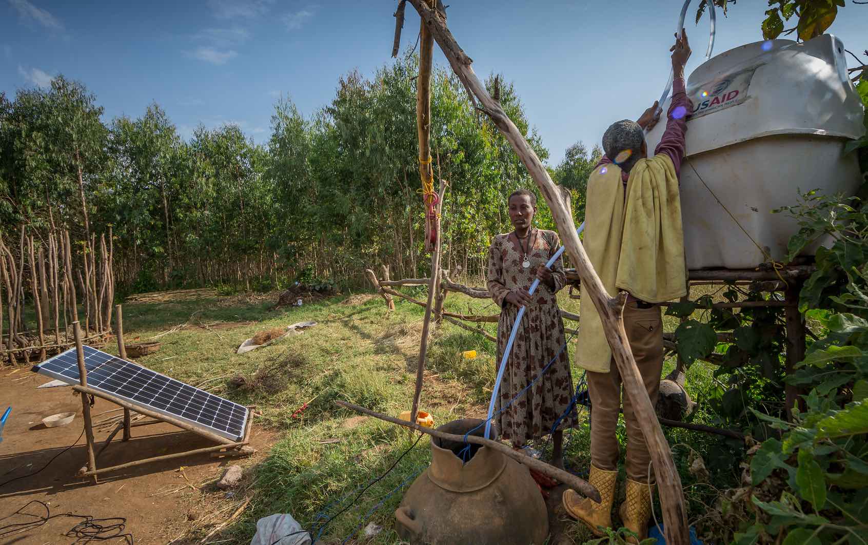 Man and woman work on water tank, right; solar panel on left