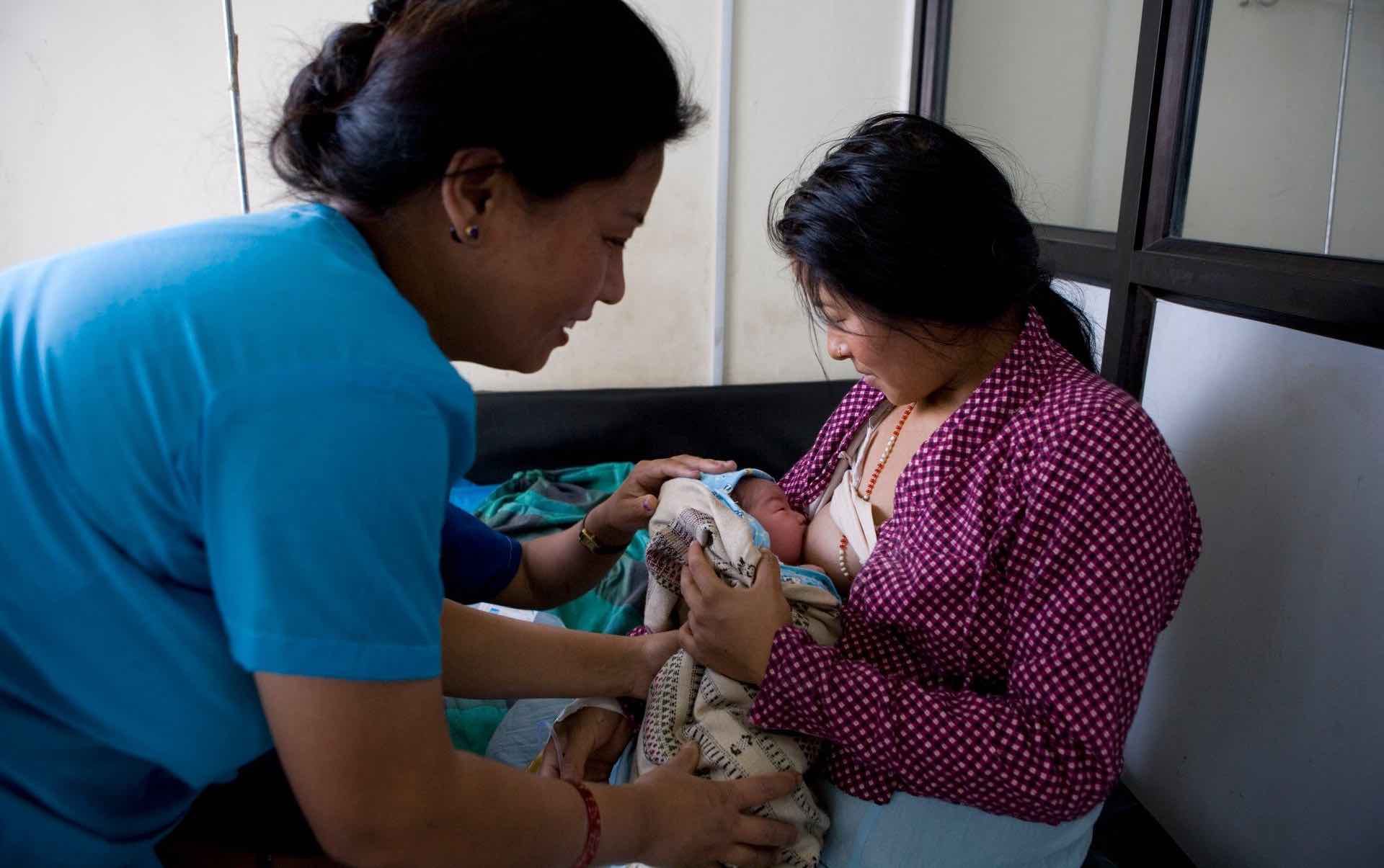 Woman breastfeeds baby while another woman helps her