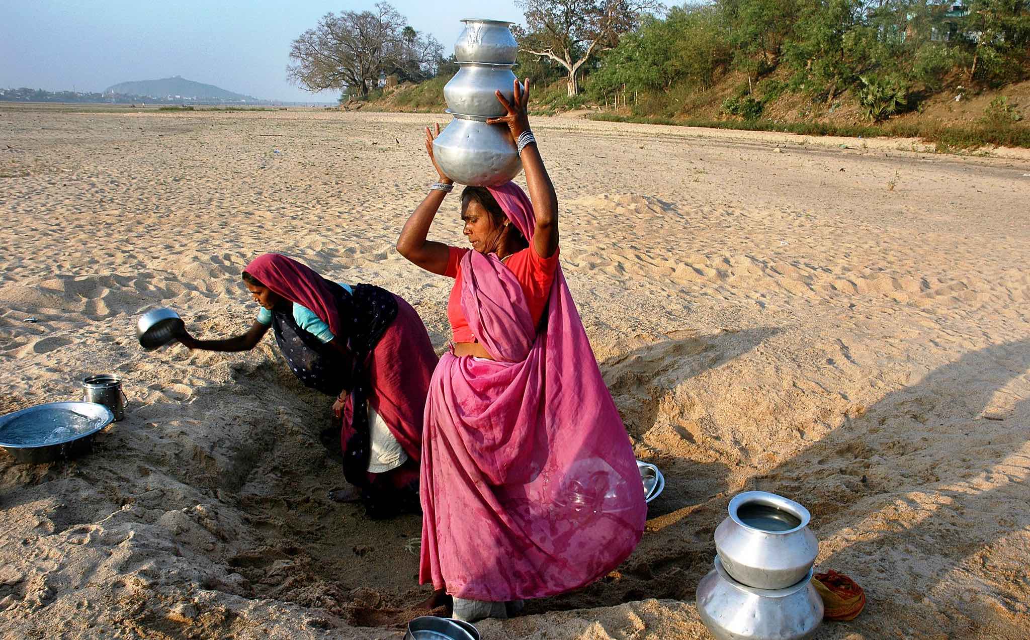 Women on left crouching with pan; women right with three water just on her head, standing in sand