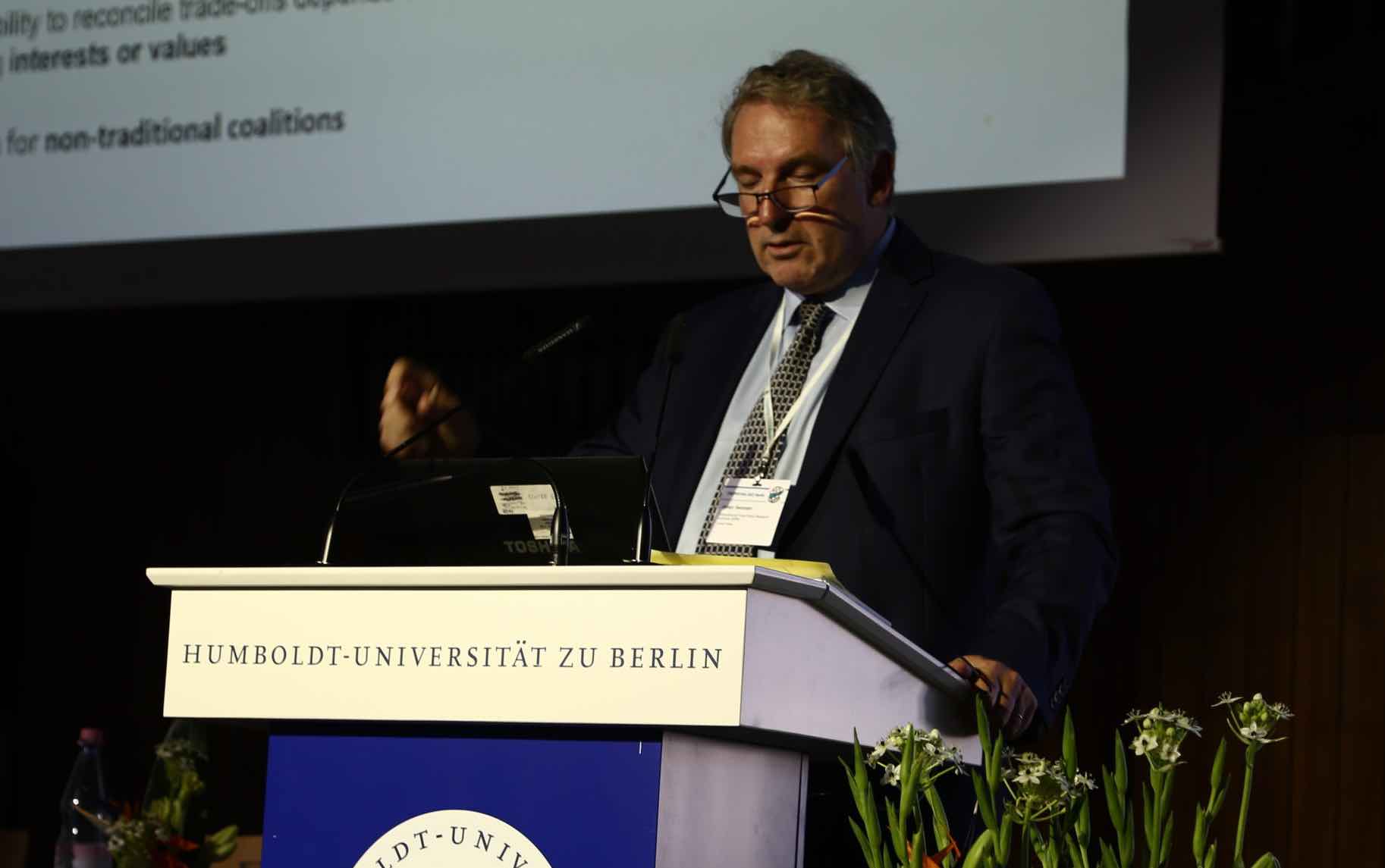 Johan Swinnen speaks from a lectern with screen