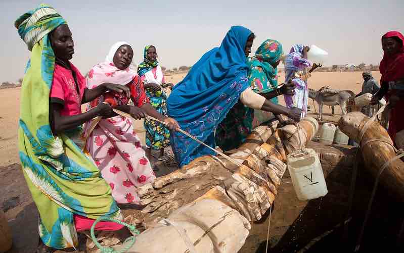 Women pulling water jugs on ropes out of well