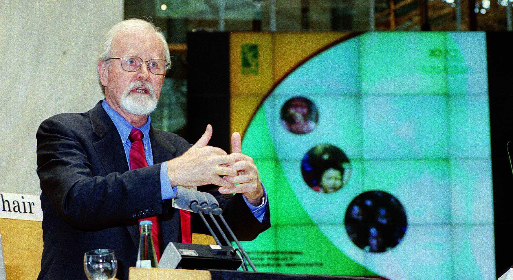 Man standing at lectern gestures with hands together