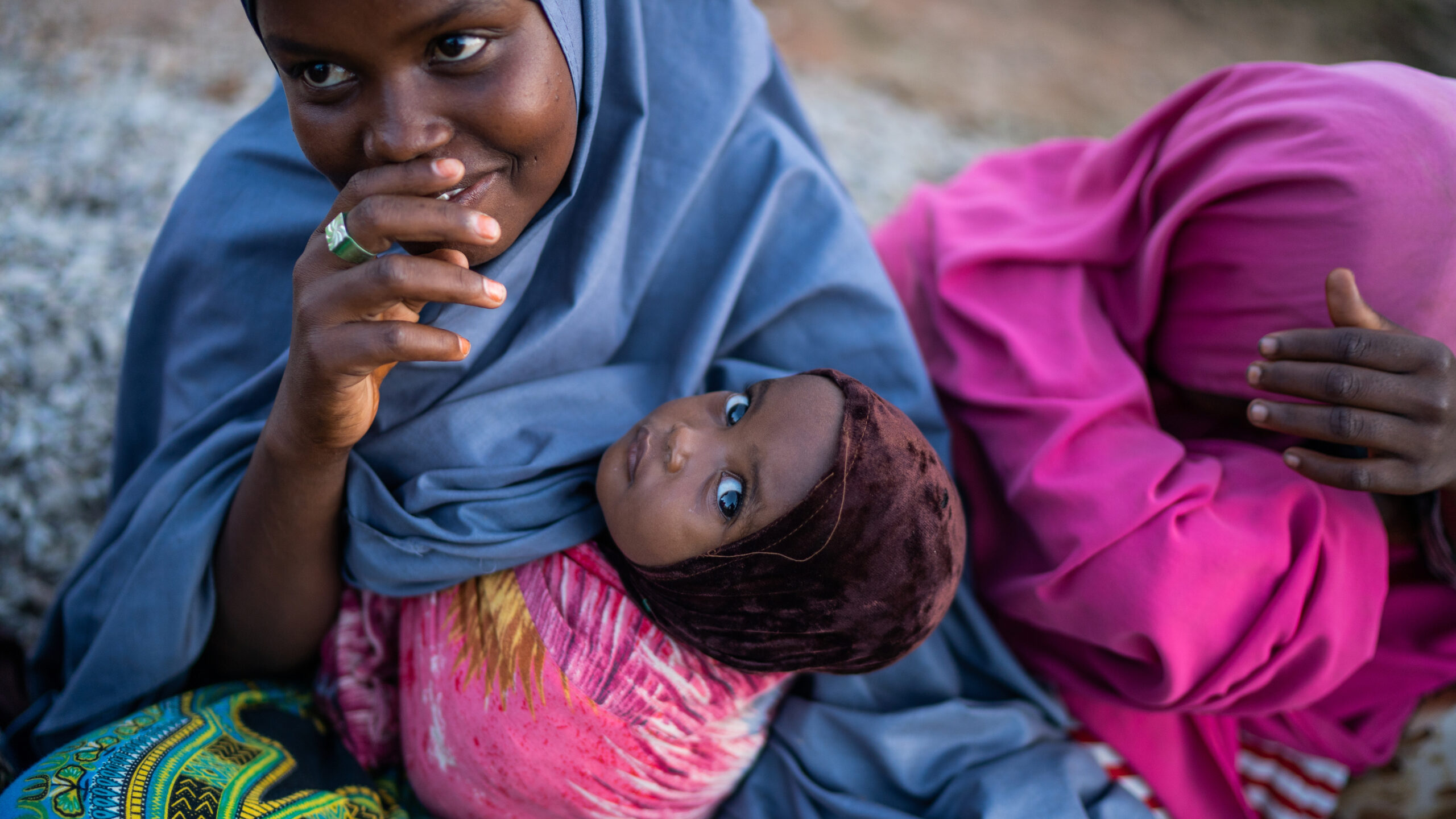 Woman, left, holds baby, who looks at camera; woman, right, head down.