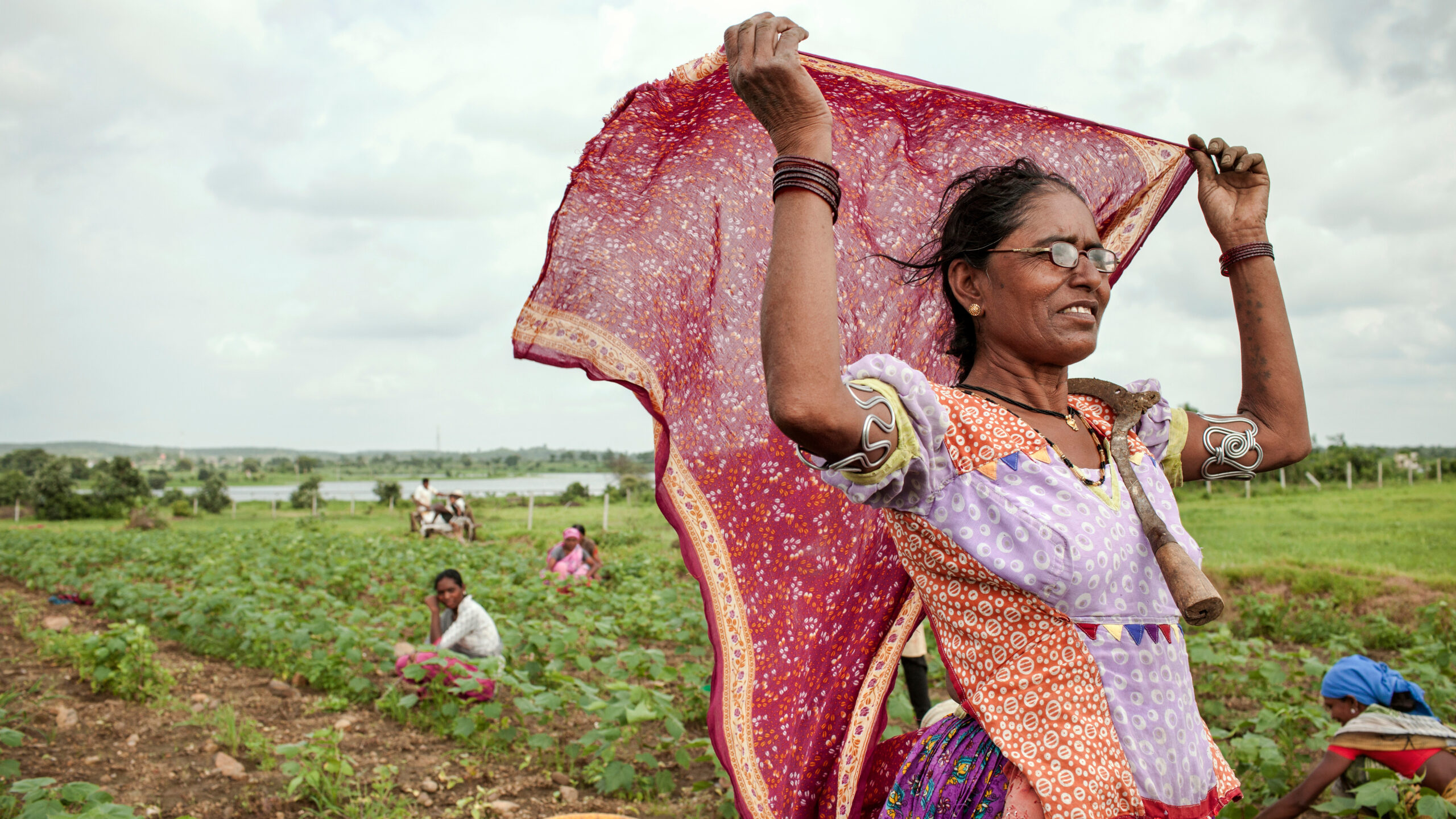 Woman standing in field, facing right, holding scarf in the air behind her.