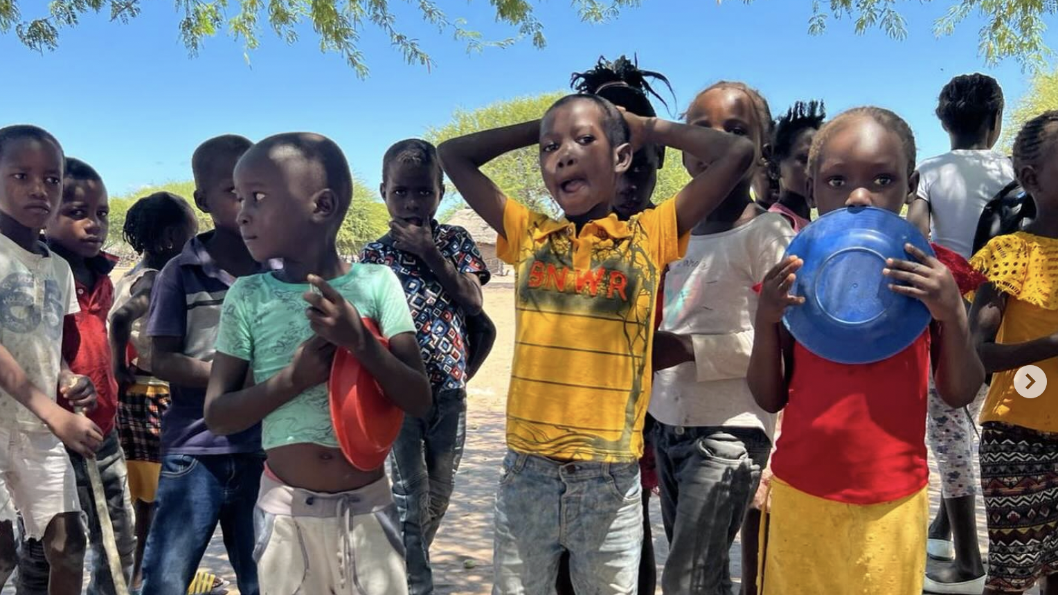 Group of children outdoors, some holding plastic bowls, facing camera.