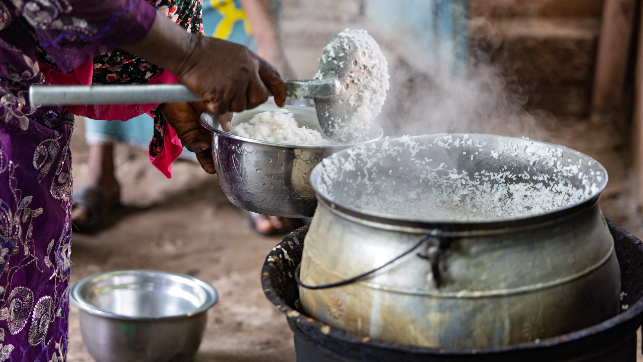 Closeup on woman holding bowl and spoon next to cauldron.