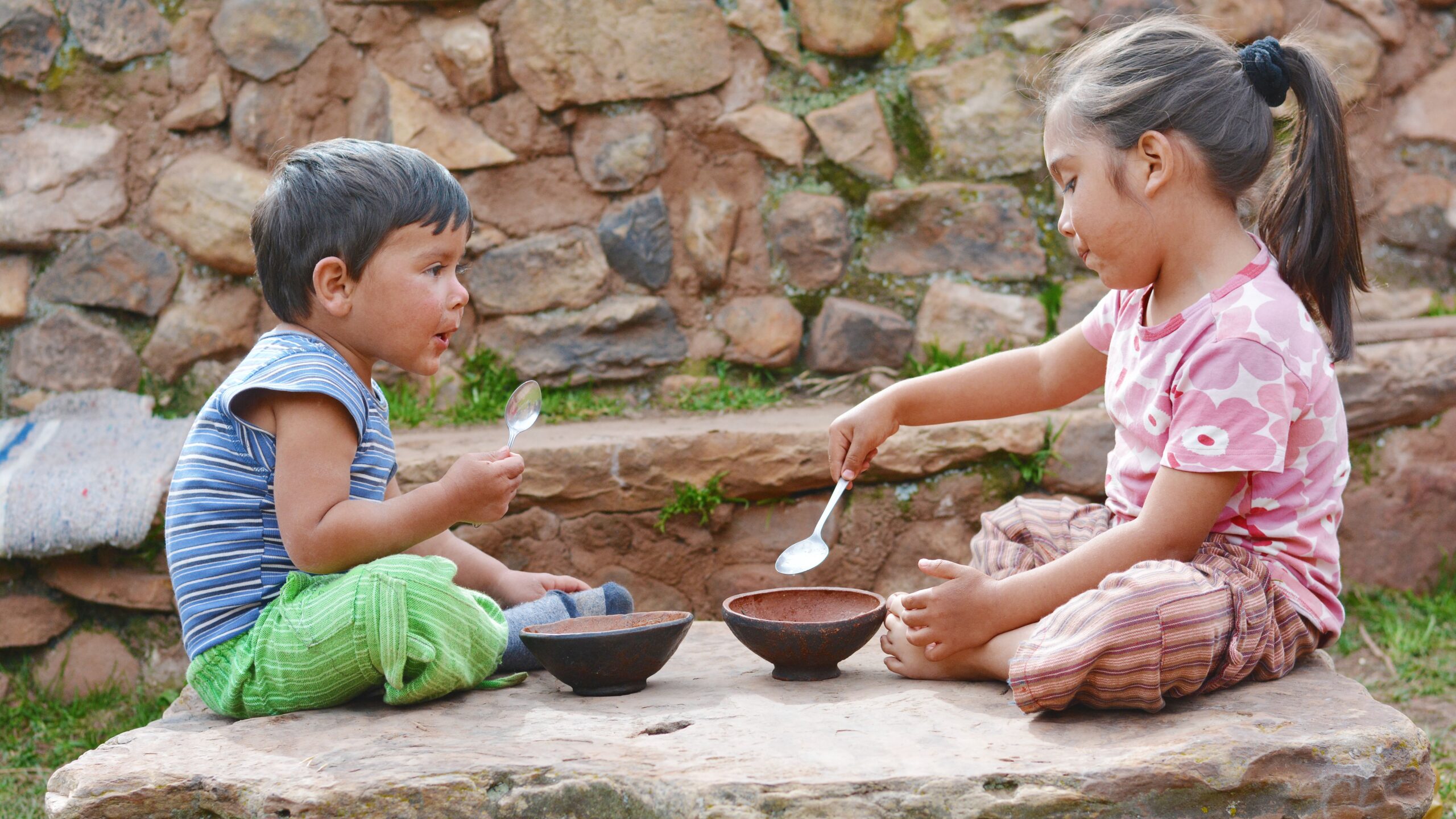 Boy and girl sitting on the big stone and eating from bowls.