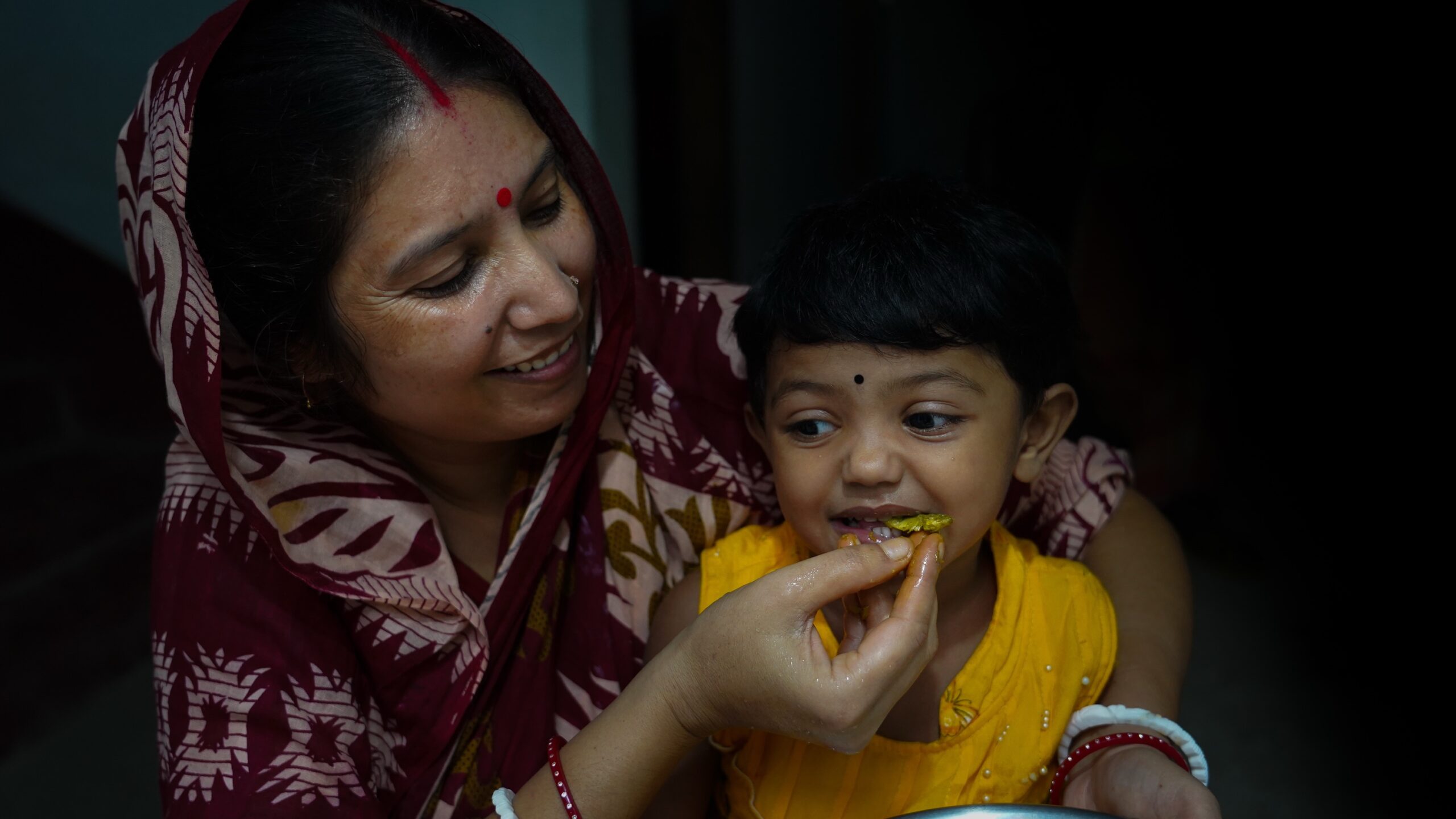 Woman feeds a fish to a child in her arms.