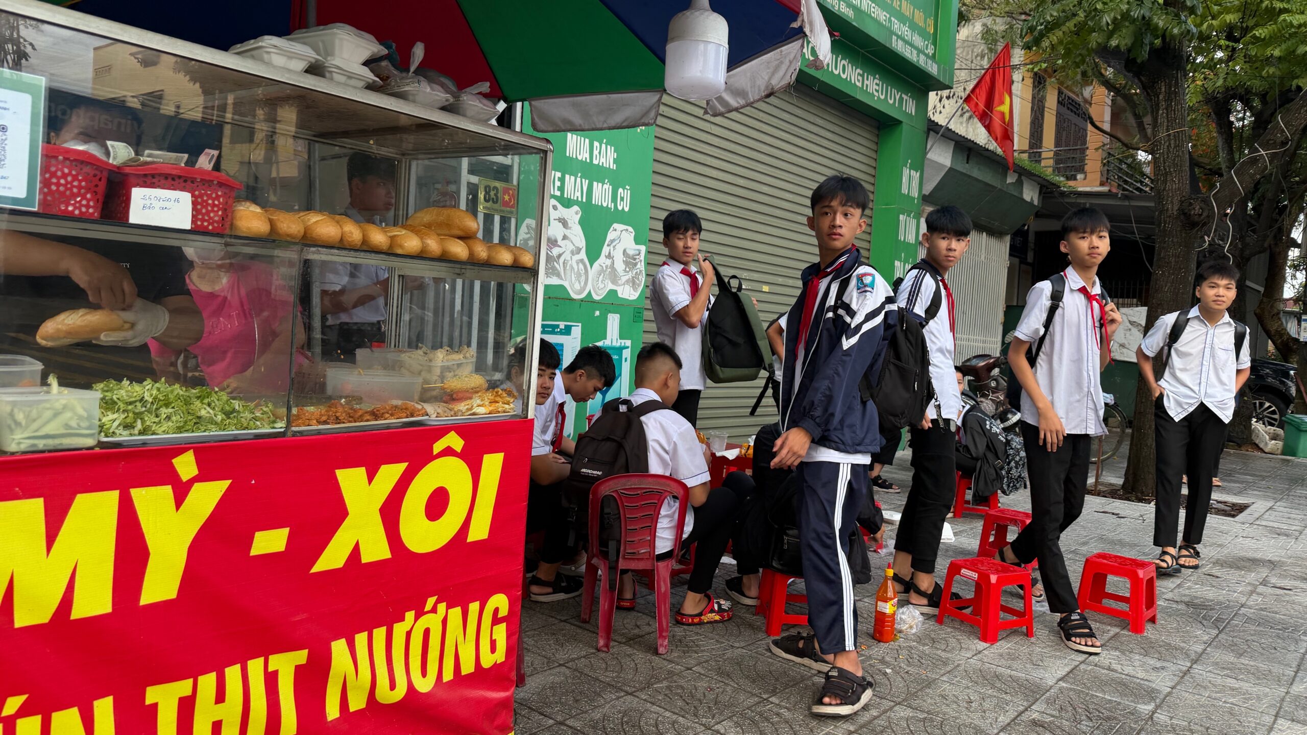 Teen boys in school uniforms standing on sidewalk next to food cart.